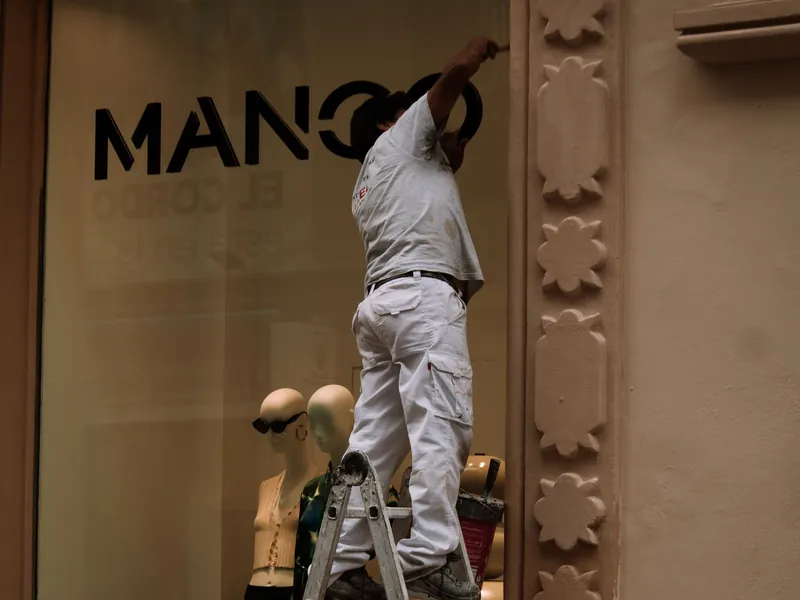 Profissional sobre uma escada reformando a fachada de um estabelecimento comercial — imagem ilustrativa.