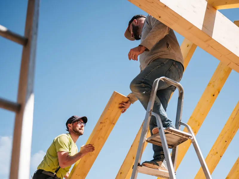 Dois trabalhadores montando a estrutura de madeira de um telhado — imagem ilustrativa.